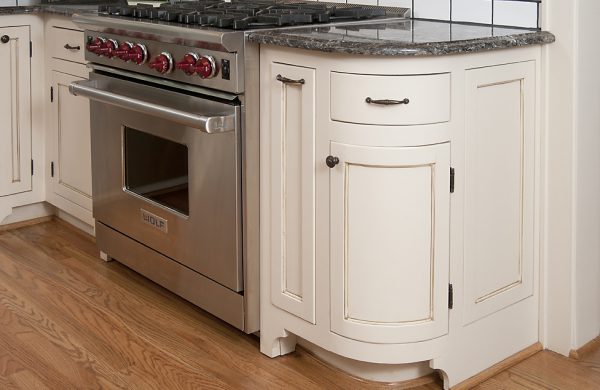 Stainless range beside white cabinetry with a rounded end cabinet