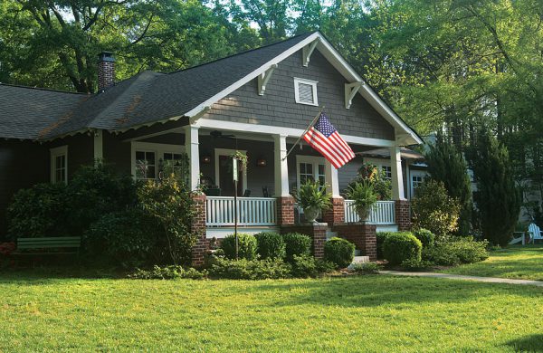 Craftsman bungalow with a covered front porch, American flag and green lawn