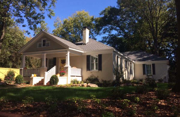 Cream custom home with a columned porch and dormers on a wooded lot