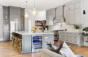 Gray kitchen with a large island, pendant lights, custom hood and wine fridge