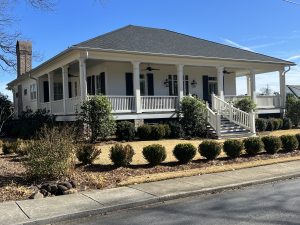White custom home with a wraparound porch and metal roof, viewed from the street